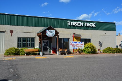 Exterior of Tusen Tack store with a sign celebrating 25 years, featuring a wooden entrance and benches outside.