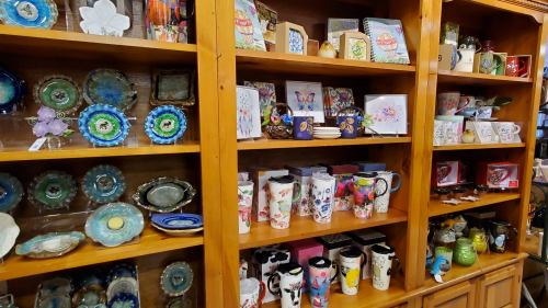 Colorful handmade pottery, mugs, and art displayed on wooden shelves in a cozy shop.