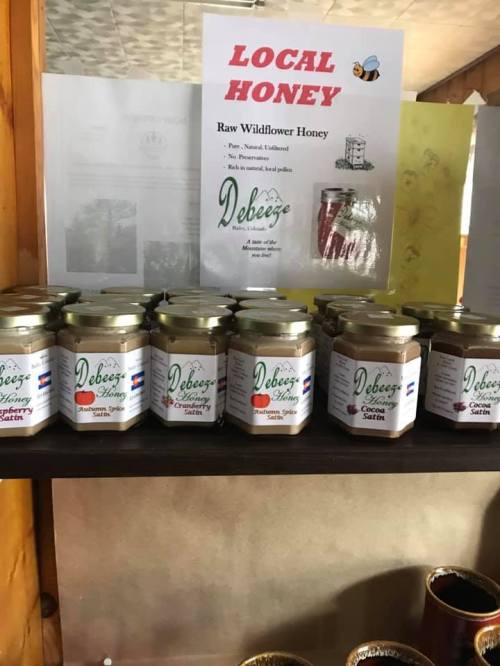 A shelf displaying jars of Debeez raw wildflower honey, with a sign promoting local honey products.