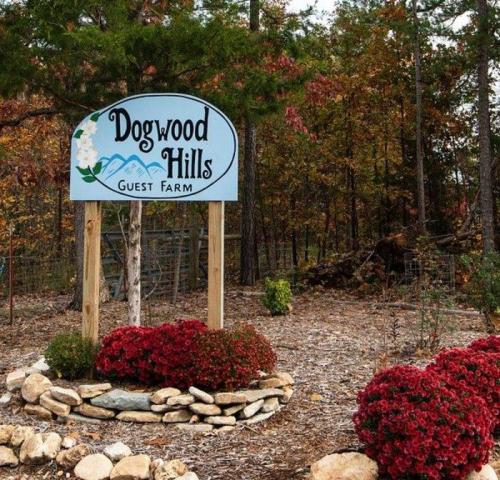 Sign for Dogwood Hills Guest Farm surrounded by colorful flowers and trees in a wooded area.