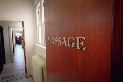 A wooden door with the word "MASSAGE" engraved, leading to a hallway in a serene setting.