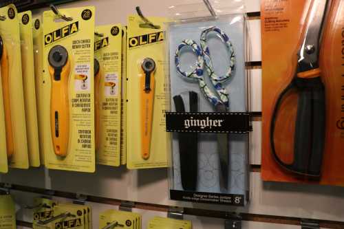 A display of crafting tools, including rotary cutters and decorative scissors, hanging on a wall.