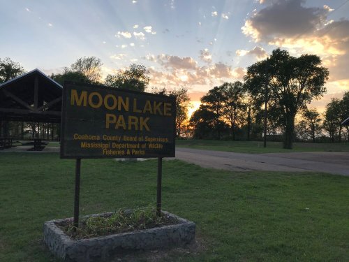 Sign for Moon Lake Park at sunset, with trees and a pavilion in the background.