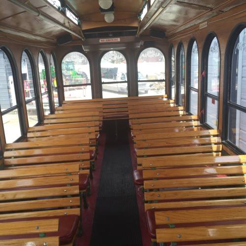 Interior of a vintage trolley with wooden benches and large windows, empty and well-lit.