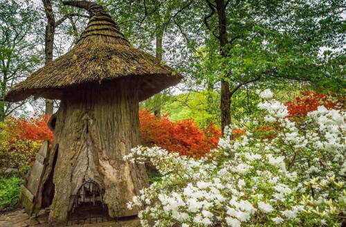 A whimsical treehouse with a thatched roof surrounded by vibrant flowers and lush greenery.
