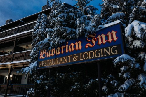 Sign for Bavarian Inn Restaurant & Lodging, surrounded by snow-covered trees and a rustic building in winter.
