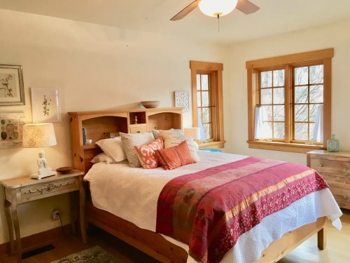 Cozy bedroom with a wooden bed, colorful throw pillows, and large windows letting in natural light.