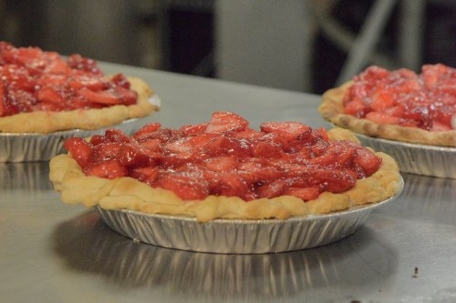 Three strawberry pies with a glossy red filling on a silver countertop.
