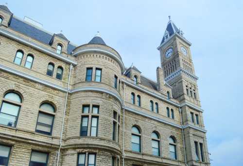 Historic stone building with a clock tower, featuring arched windows and a slate roof against a cloudy sky.