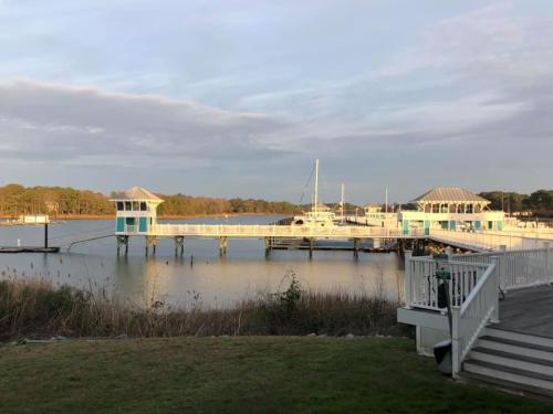 A serene waterfront scene featuring a wooden pier with two gazebos, boats docked, and calm water under a cloudy sky.