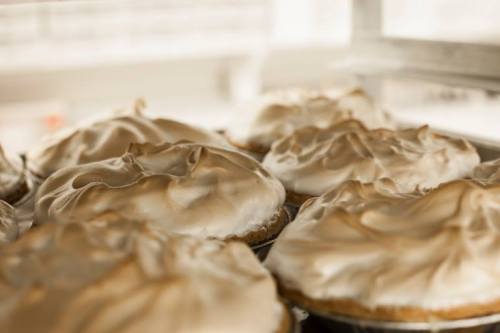 Close-up of several golden-brown meringue-topped pies in a display case.