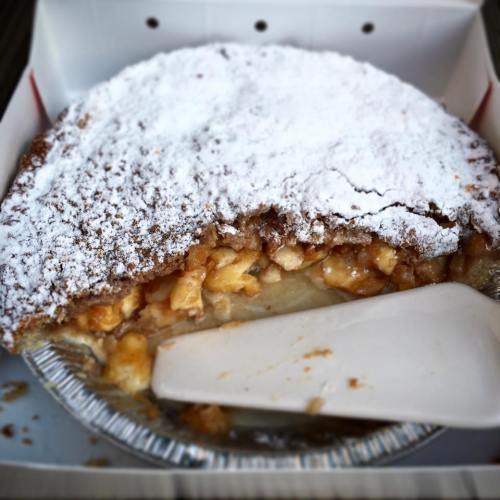 A partially sliced apple pie dusted with powdered sugar, sitting in a pie tin with a serving spatula beside it.