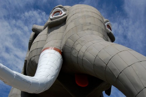 A large, whimsical elephant statue with a prominent trunk and bright eyes against a blue sky.