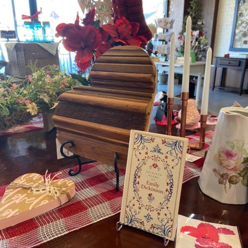 A wooden heart-shaped box, a card about Emily Dickinson, and decorative items on a table with a red checkered cloth.