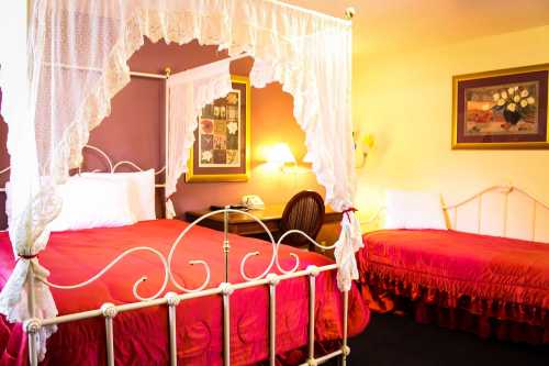 A cozy bedroom featuring a canopy bed with red bedding and a second smaller bed, adorned with decorative pillows.