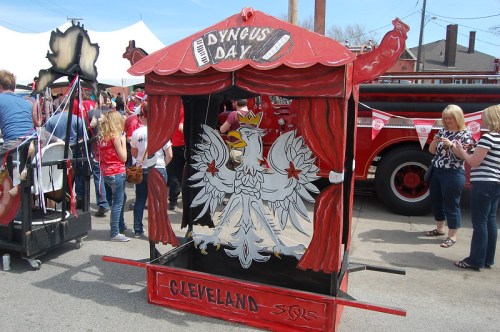 A colorful puppet stage decorated with a white eagle, celebrating Dyngus Day in Cleveland, surrounded by festival-goers.