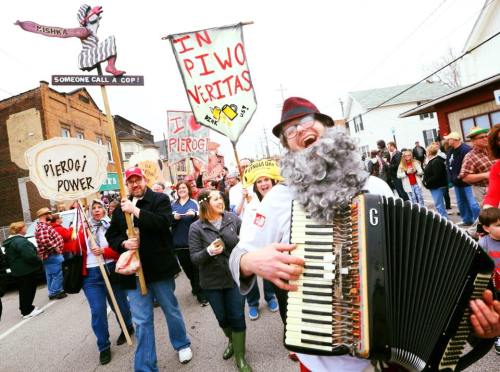 A lively parade scene with people holding signs, a musician playing accordion, and a festive atmosphere celebrating pierogi.