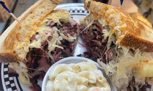 A close-up of a sandwich filled with layers of meat and sauerkraut, served with a side of macaroni salad.