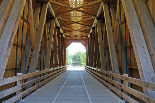 A wooden covered bridge interior with a symmetrical design, leading to an open area at the far end.