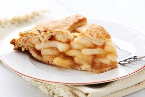 A slice of apple pie on a white plate, showcasing layers of sliced apples and a golden, flaky crust.