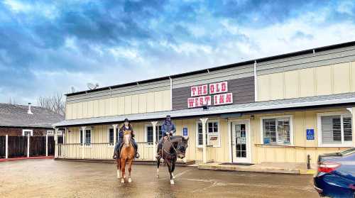 Two people on horseback in front of a building labeled "The Old West Inn" under a cloudy sky.