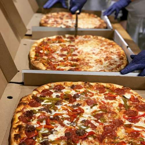 Three large pizzas in boxes, one being sliced, topped with pepperoni, cheese, and colorful bell peppers.