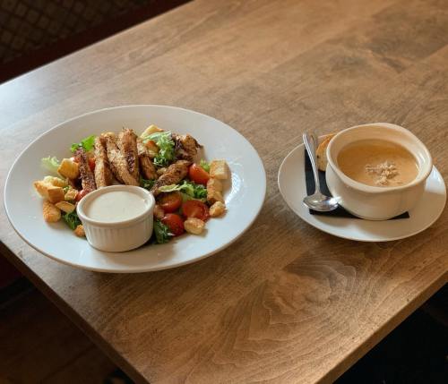 A plate with grilled chicken salad and a bowl of creamy soup on a wooden table.