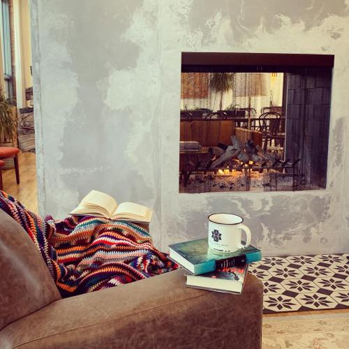 Cozy living space with a colorful blanket, a stack of books, and a steaming mug by a modern fireplace.
