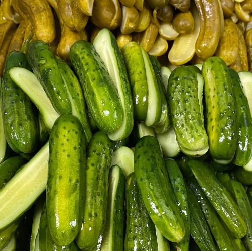 A close-up of fresh green cucumbers and pickles stacked together, showcasing their vibrant colors and textures.