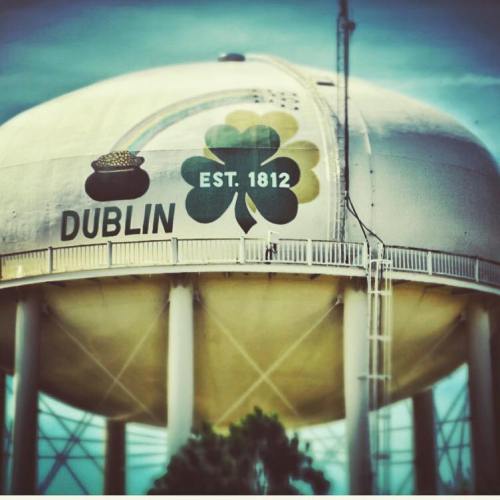 Water tower in Dublin featuring a shamrock and the text "Dublin EST. 1812" against a blue sky.