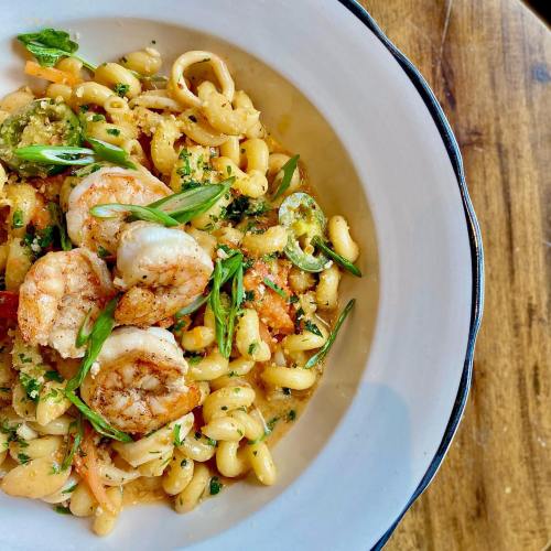 A bowl of pasta with shrimp, herbs, and vegetables, served on a wooden table.