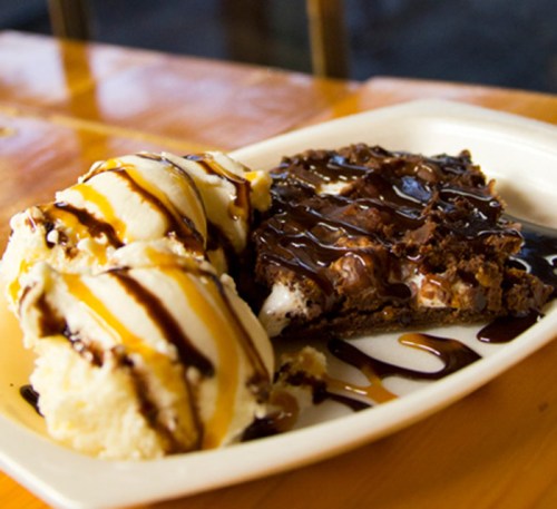 A plate with two scoops of vanilla ice cream drizzled with chocolate sauce and a warm brownie topped with chocolate syrup.