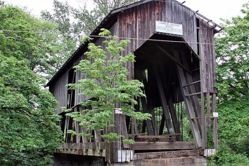 A weathered wooden covered bridge surrounded by lush green trees.