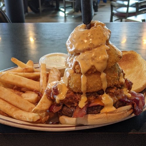 A hearty burger topped with onion rings and sauce, served with fries on a plate.