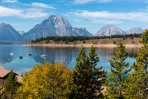 Scenic view of a calm lake surrounded by mountains and trees under a clear blue sky.