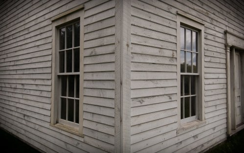 Two windows on a weathered wooden building corner, showcasing a rustic, aged exterior.