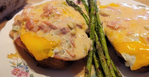A plate of cheesy toast topped with ham and asparagus, drizzled with a creamy sauce.