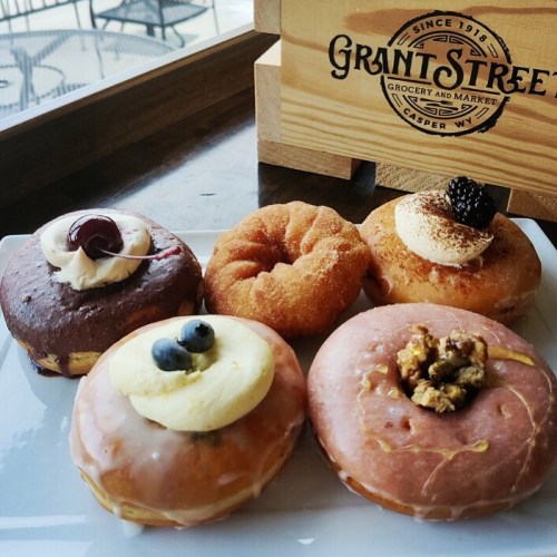 A plate of assorted donuts, including chocolate, glazed, and topped with fruit and cream, next to a wooden sign.