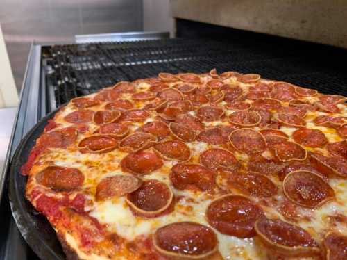 A close-up of a freshly baked pepperoni pizza on a grill, with a golden crust and abundant pepperoni slices.