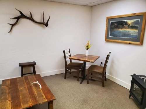 Cozy room with wooden furniture, a wall-mounted antler, a framed landscape picture, and a small vase of flowers.