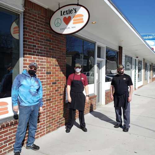 Three people in masks stand outside Lexie's restaurant in Exeter, NH, with a brick facade and a sign above.