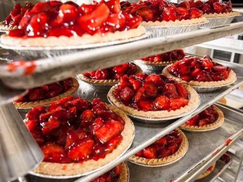A display of freshly baked strawberry pies on metal racks, glistening with red fruit filling.