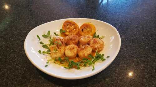 A plate of seared scallops garnished with herbs and served with grilled lemon slices on a dark countertop.