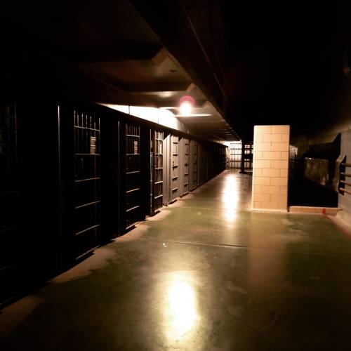 Dimly lit prison corridor with metal cell doors on either side and a solitary light illuminating the space.