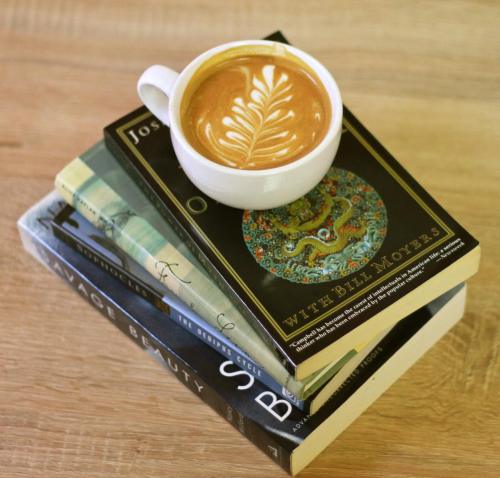 A stack of books topped with a white cup of latte art on a wooden surface.