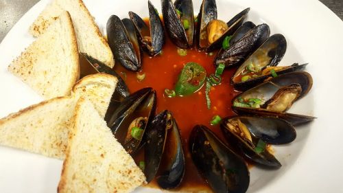 A plate of mussels in a spicy sauce, garnished with green onions, served with slices of toasted bread.