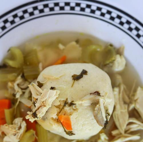A bowl of soup with a large dumpling, shredded chicken, and vegetables like carrots and celery.