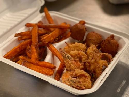A takeout container with sweet potato fries, fried shrimp, and two hushpuppies.