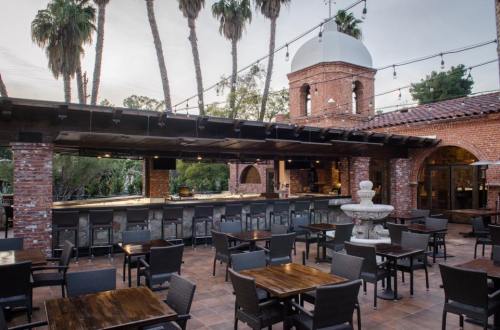 Outdoor bar area with a fountain, surrounded by palm trees and brick architecture, featuring tables and chairs.