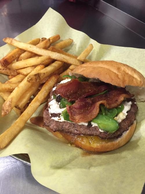 A juicy burger with bacon, lettuce, and cheese, served with a side of crispy French fries on a green paper tray.